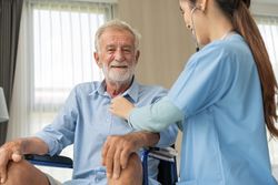 Smiling older male in wheelchair having chest examined by Asian nurse