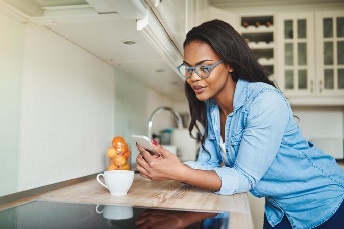 Woman checking phone leaning on kitchen counter