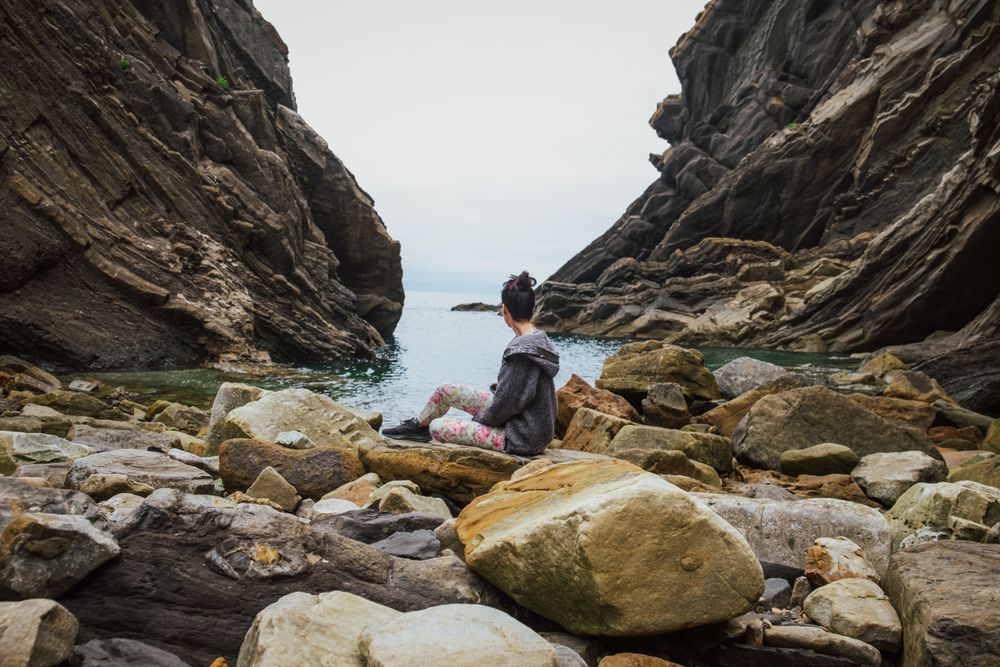 Woman on boulders shore against gorge and seascape in overcast weather