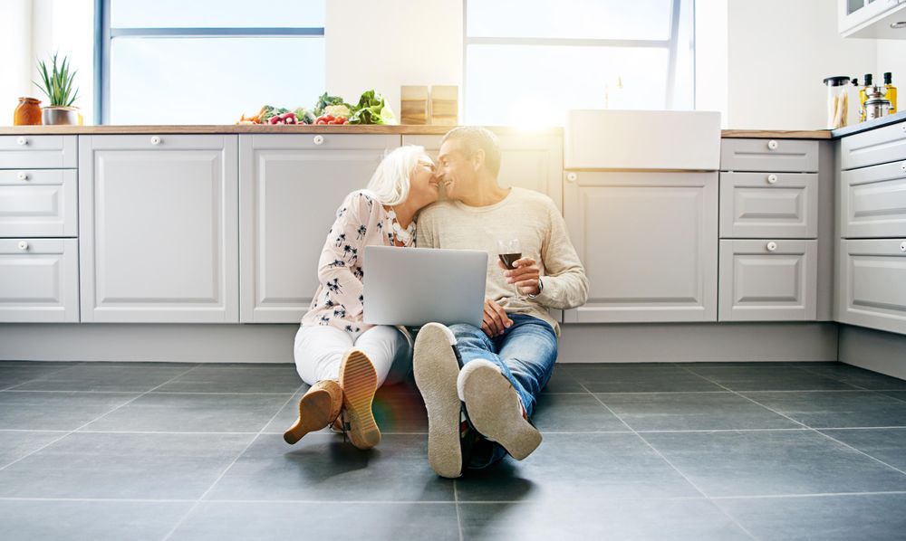 Older couple relaxing on kitchen floor with wine and computer