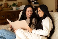 Mature mother and adult daughter smiling while they are watching a photo album