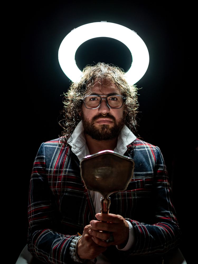 Serious man with glowing fake nimbus holding mirror and looking at camera