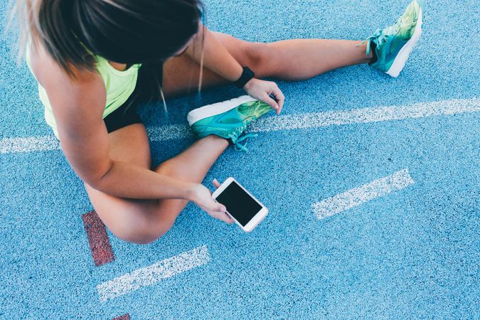 Woman stretching on a track field with phone