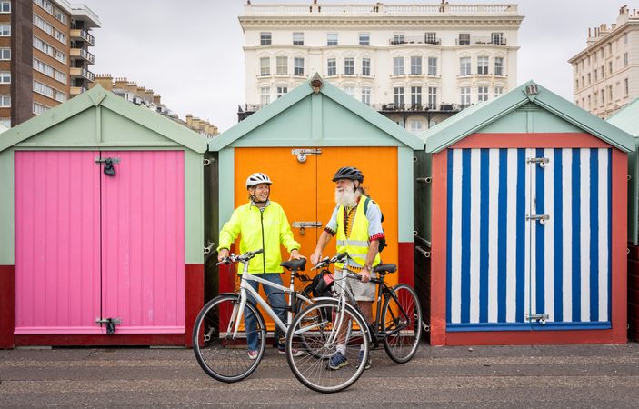 Two older people standing and talking with bikes in front of bright sheds