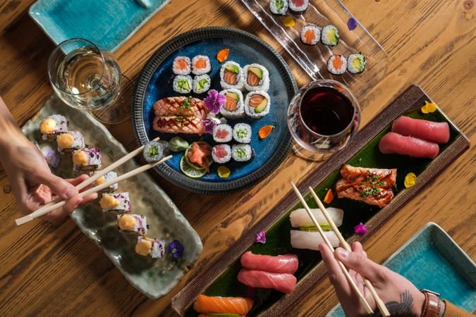 Anonymous couple eating various sushi with wine