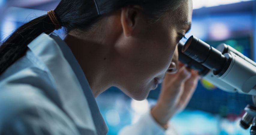 Medical Development Laboratory: Close Up Portrait of Asian Female Scientist Using Microscope, Analyzes Petri Dish Sample.