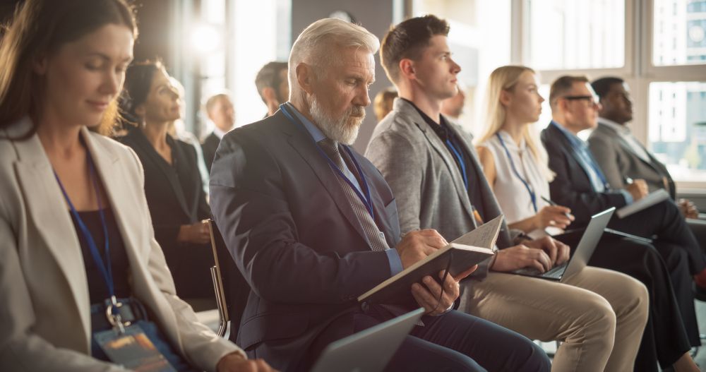 White Man Sitting in a Crowded Audience at a Business Forum. Corporate Delegate Taking Notes. Successful Male CEO Attending Business Conference, Listening To Presentation.