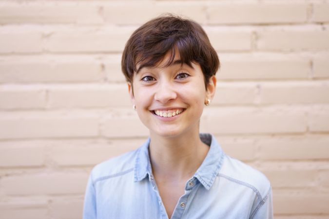 A Cheerful Young Woman with Short Hair is Smiling Brightly Against a Neutral Background