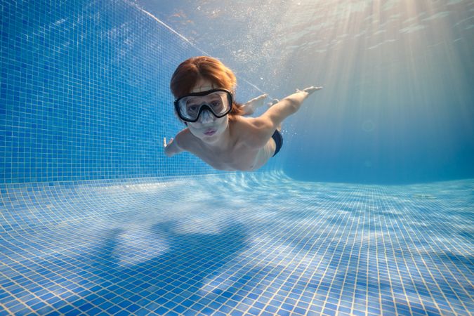 Small boy in mask swimming underwater of pool