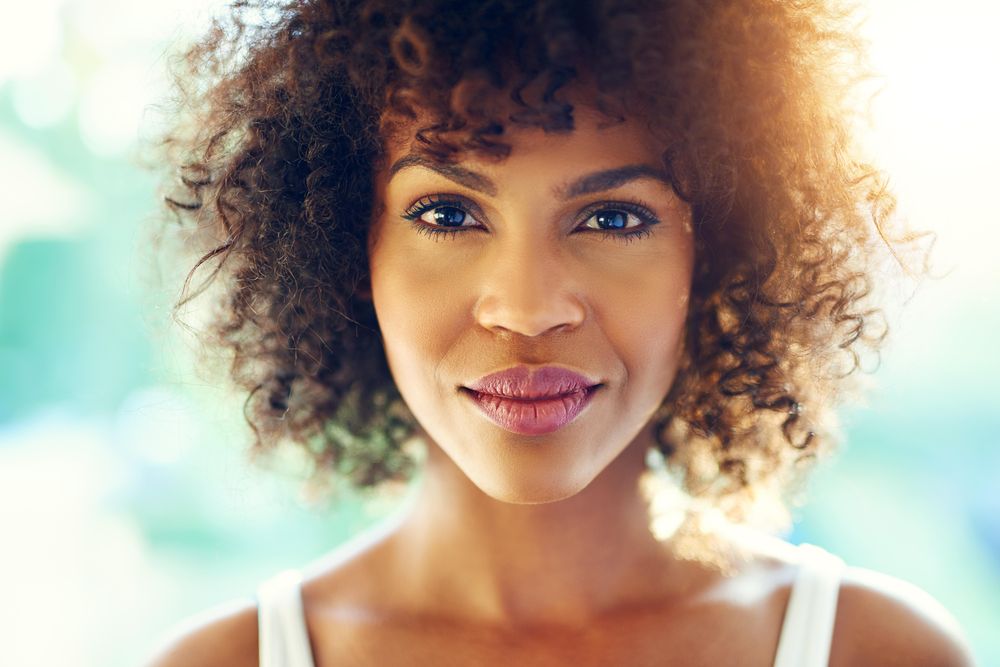 Close up portrait of female with curly hair on blurry leafy background