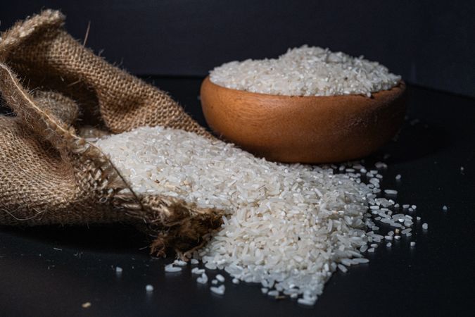 rice spilling from a burlap sack onto a dark surface