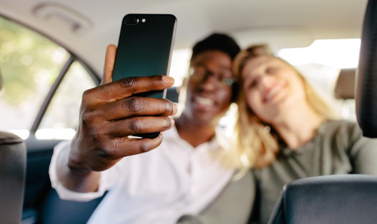 Couple sitting in back seat of a car and taking selfie