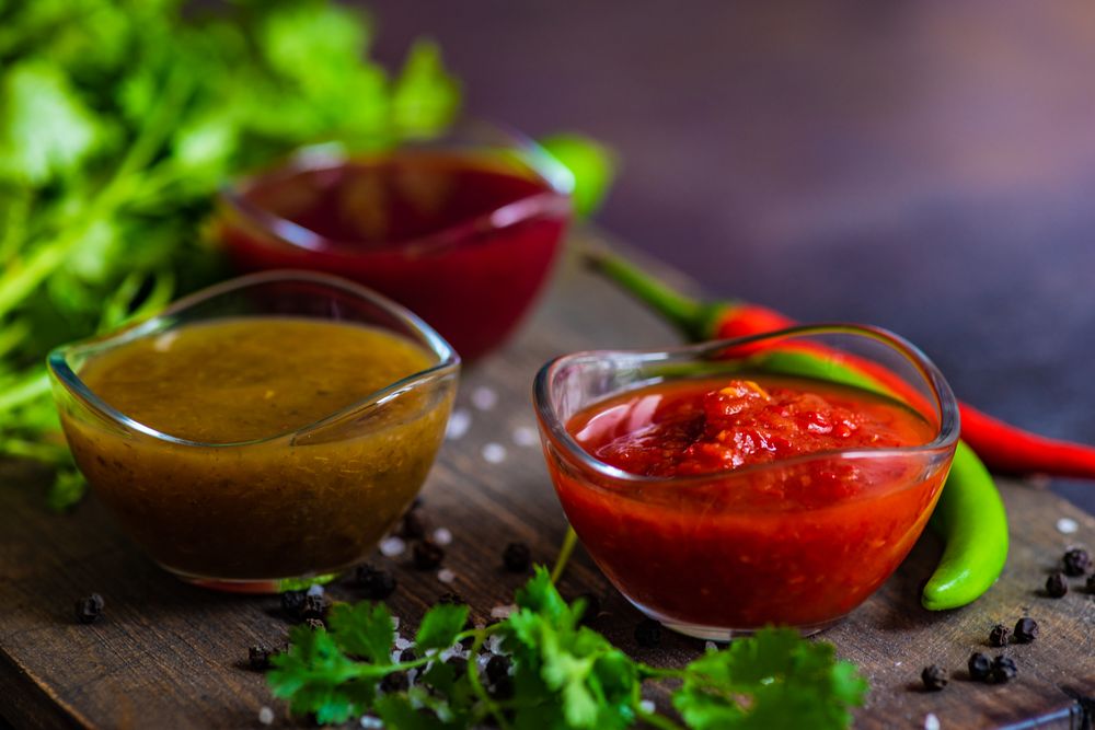 Side view of three traditional Georgian condiments tomato satsebeli, yellow and red tkemali with ingredients on cutting board