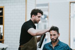 Barber doing hairstyle to man in salon