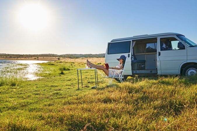 Woman sitting on chair near table and reading book on shore of river