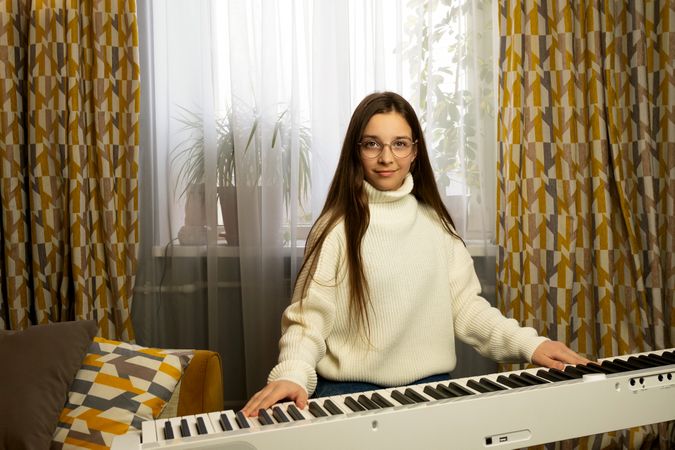 Girl in glasses sitting at piano, looking at camera