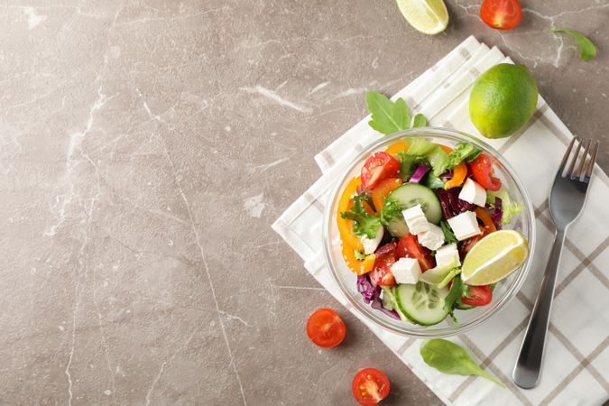 Salad, fork and kitchen towel on grey background, top view