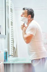 Man shaving beard with razor in bathroom