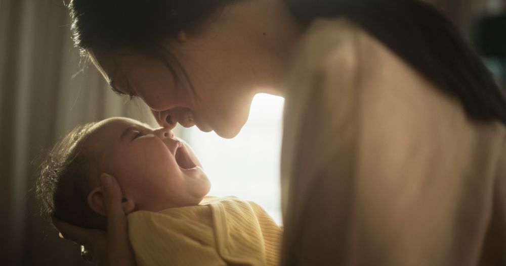 Motherly Affection Concept: Close Up Portrait of a Cute Asian Baby Laughing and Enjoying Bonding Time Together, Looking at Mother with Love.