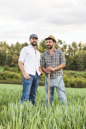 Two men in plaid shirt standing in long grass field with forest in background