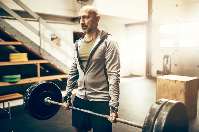 Fit man in grey hoodie holding heavy barbell