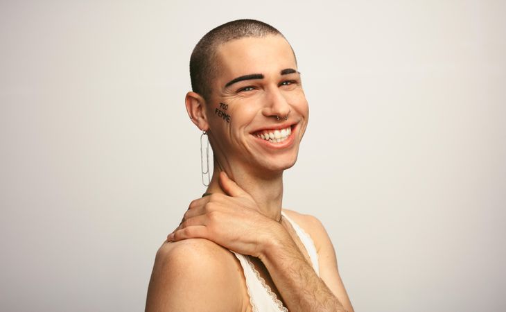 Portrait of a young man wearing earring looking happy on light background