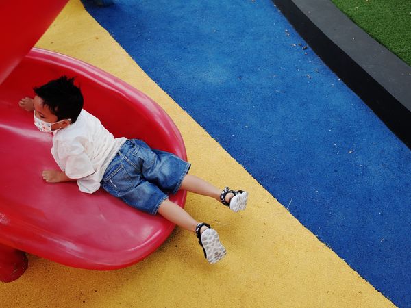 Boy with facemask on red slide in playground