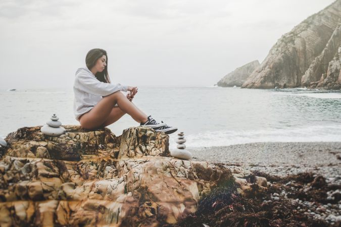 Woman taking selfie on smartphone on shore near stones and water