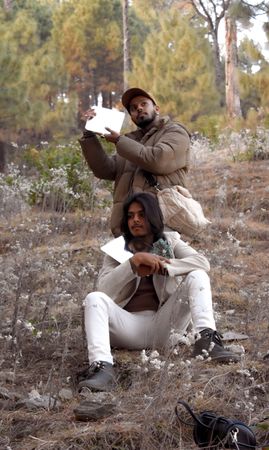 Two men holding square mirror outdoor near trees