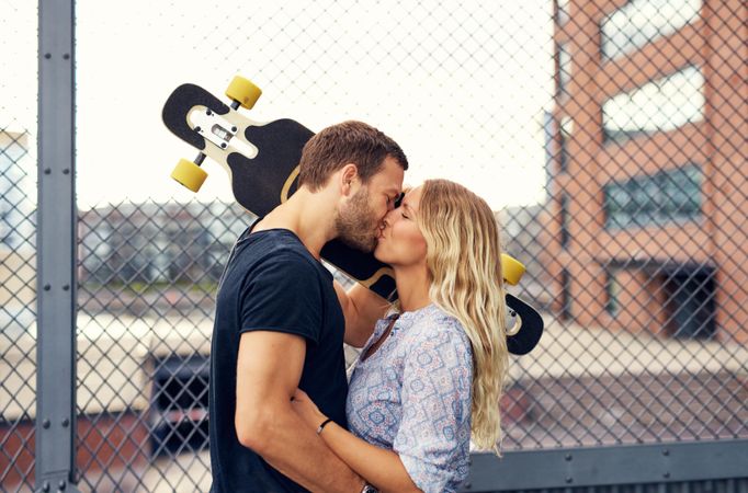 Man and woman kissing with man holding skateboard to shoulder