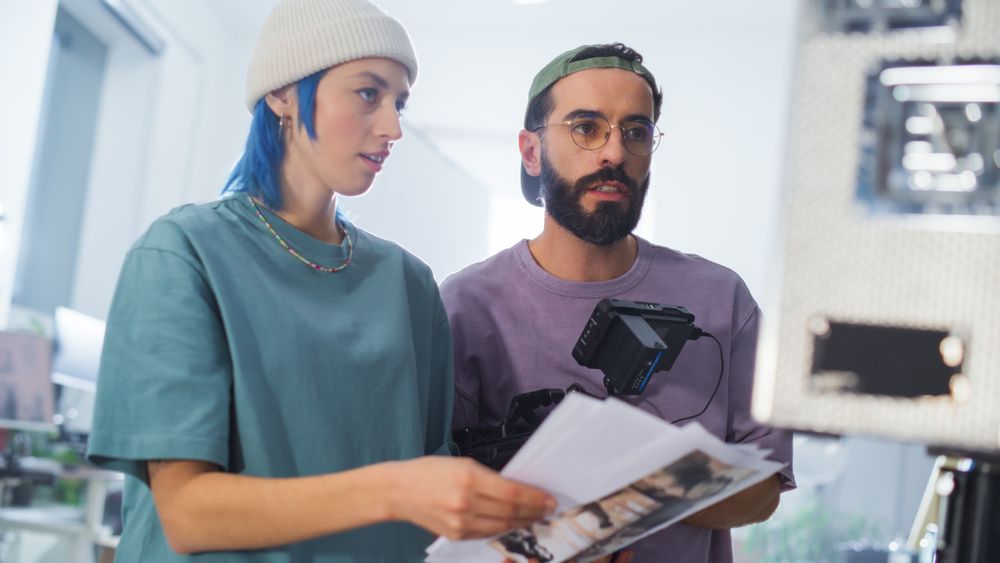 Young Female And Middle Eastern Male Cinematographers Review A Script By A Camera On A Modern Film Set, Showcasing Teamwork In Video Production For A Documentary Or Tv Show.