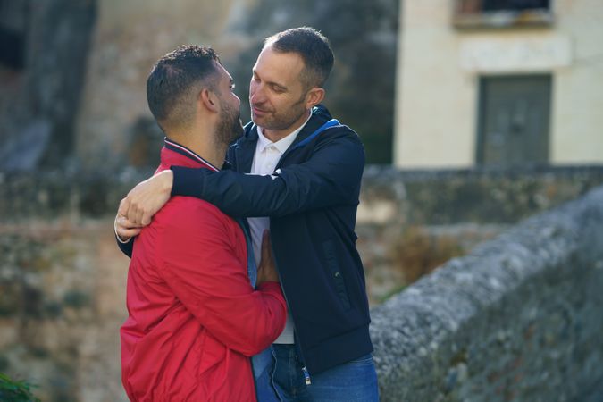 Two men hugging each other near stone wall outside