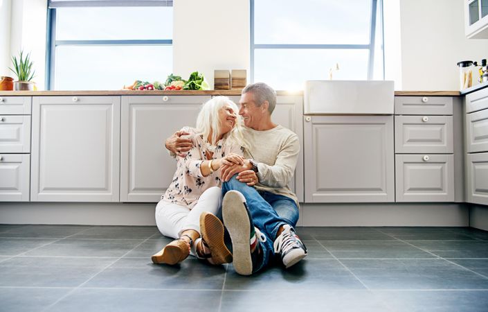 Relaxed grey haired couple sitting on the tiles of the kitchen floor