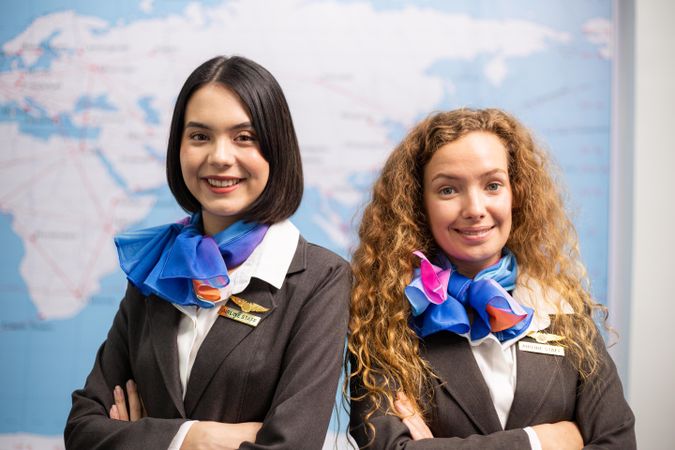 Two women flight attendants standing in front of map and smiling