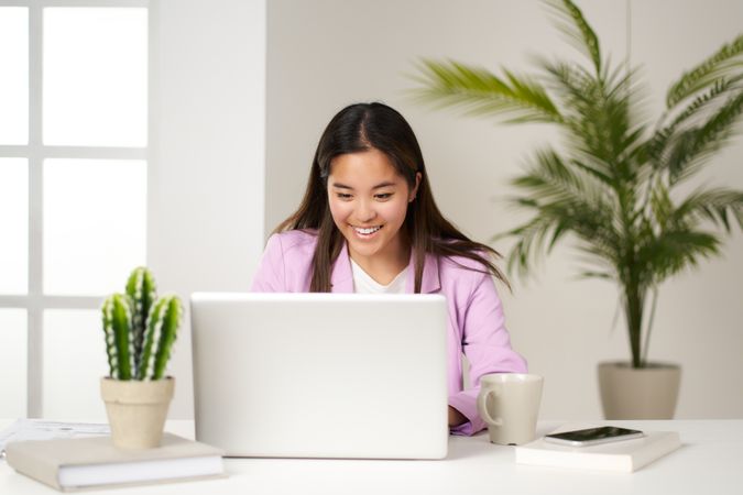 a young asian woman smiling and looking at the computer in the coworking space
