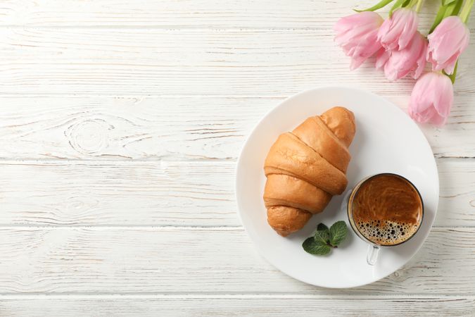 Plate with croissant on wooden table with tulips, copy space