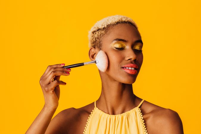 Black woman with short blonde hair applying blush to cheek