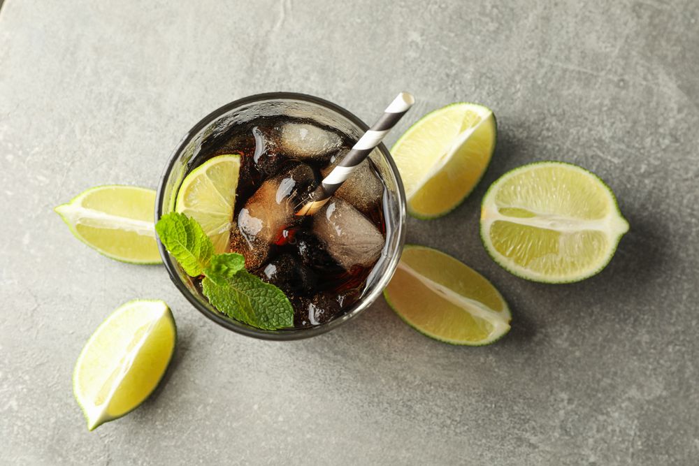 Glasse with cold cola and citrus on grey table, top view