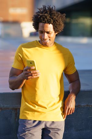 Black man in yellow t-shirt checking his smart phone in the sun, vertical