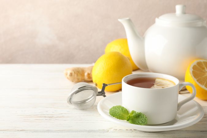 Cup of tea with lemon, mint, strainer, ginger and teapot on wooden background, copy space