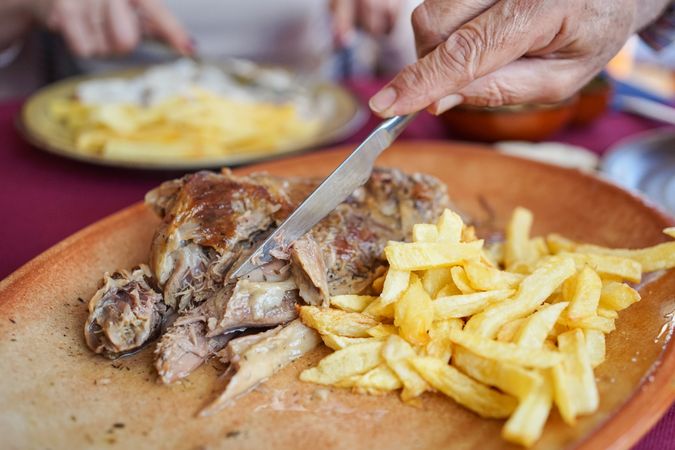 Faceless woman eating fries with meat in sauce in restaurant