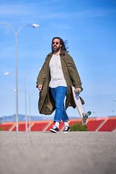 Trendy hipster man in raincoat walking with skateboard