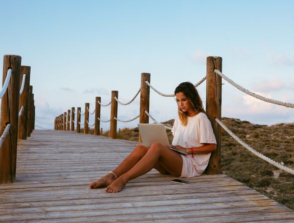 Smart resting woman remote worker using laptop while lying on bridge