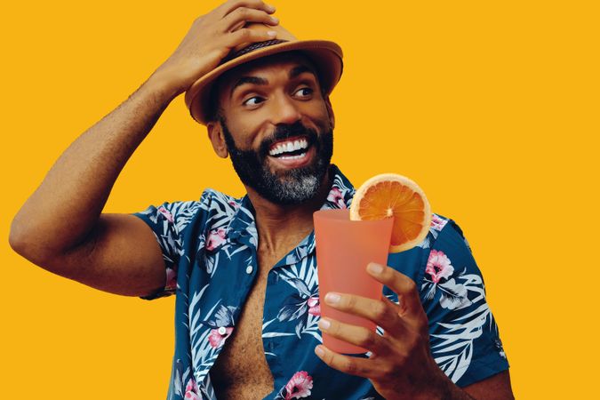 Smiling male wearing colorful shirt and looking away from cocktail with yellow background