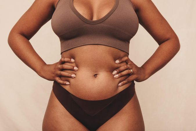 Unrecognizable woman standing with her hands on her tummy in a studio wearing brown undergarments