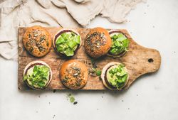 Fresh vegan burgers on seeded buns arranged on wooden bread board