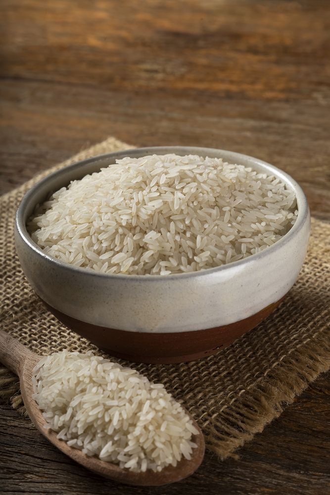 Rice in a ceramic bowl on brown wooden background.