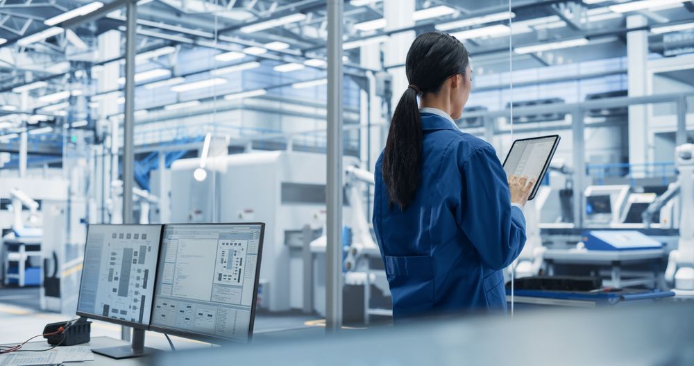 Factory Chief Technical Officer Working on Tablet at a Futuristic Industrial Manufacture with Autonomous Robotic Assembly Line. Specialist Monitoring Production, Planning Work for Employees
