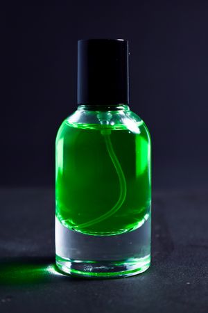 Green perfume bottle in dark studio with copy space