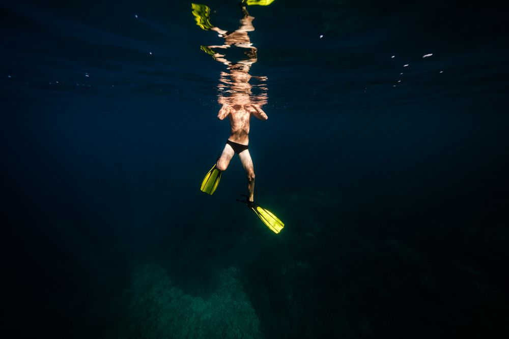Anonymous fit man swimming undersea in sunlight